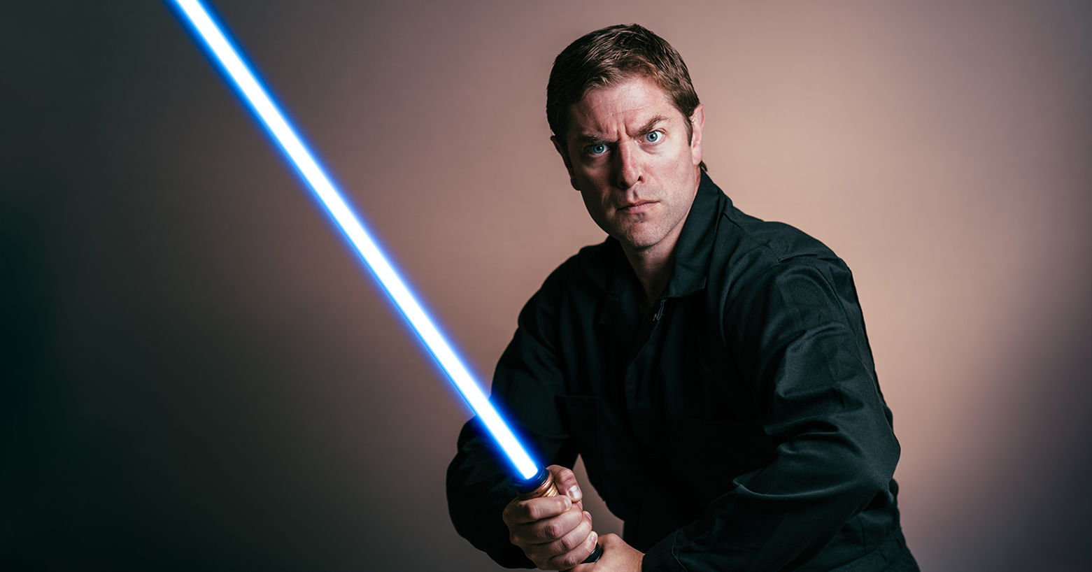 Photo of Charles Ross dressed as a Jedi, holding a blue lightsaber.