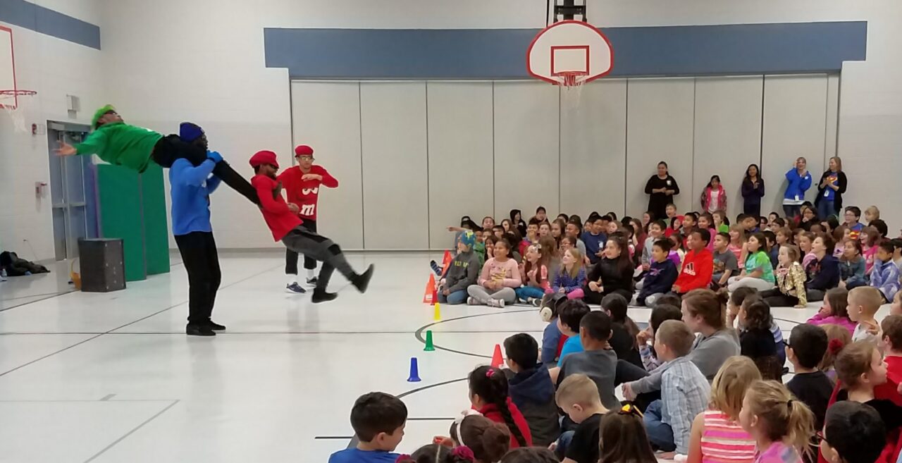Dancers doing acrobatics in a school gym for a school assembly.