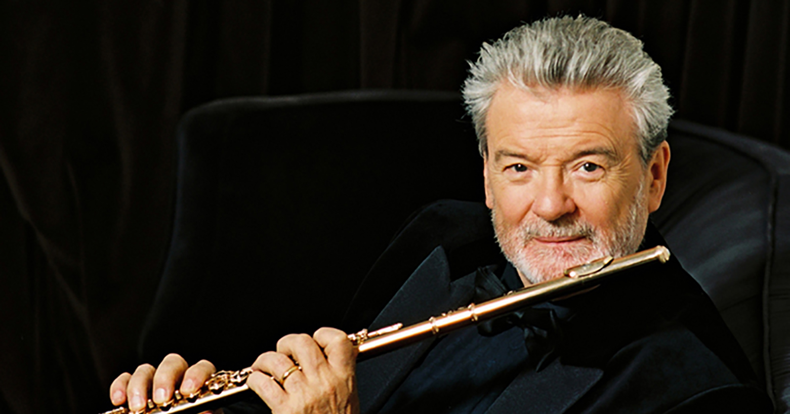 Sir James Galway holding a flute and smiling.