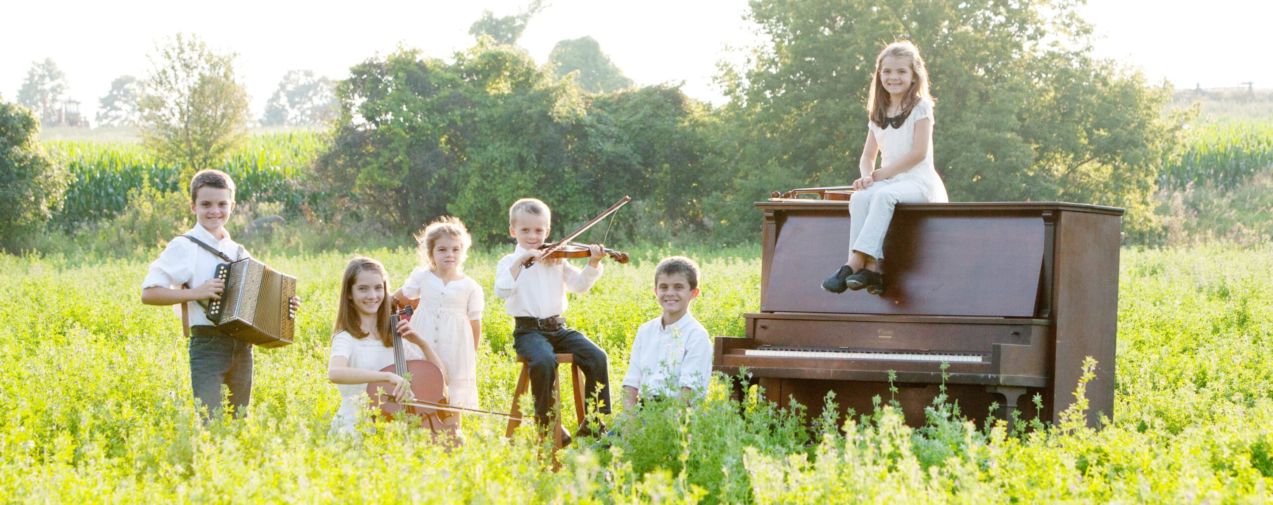 The Leahy children sitting on a piano in the middle of a field.