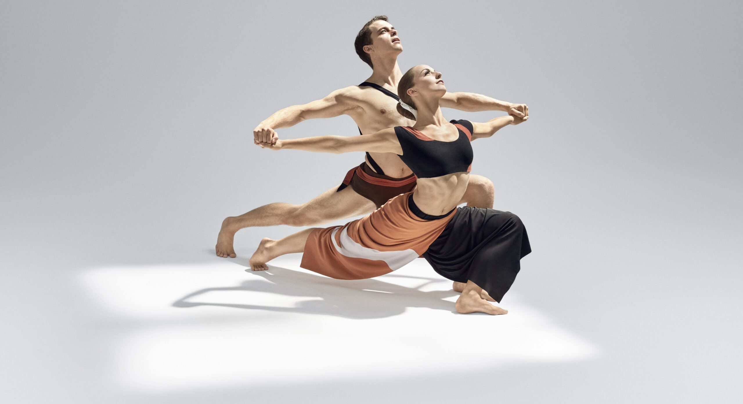 Two dancers from the Dark Meadow Suite dancing low in front of a white background.