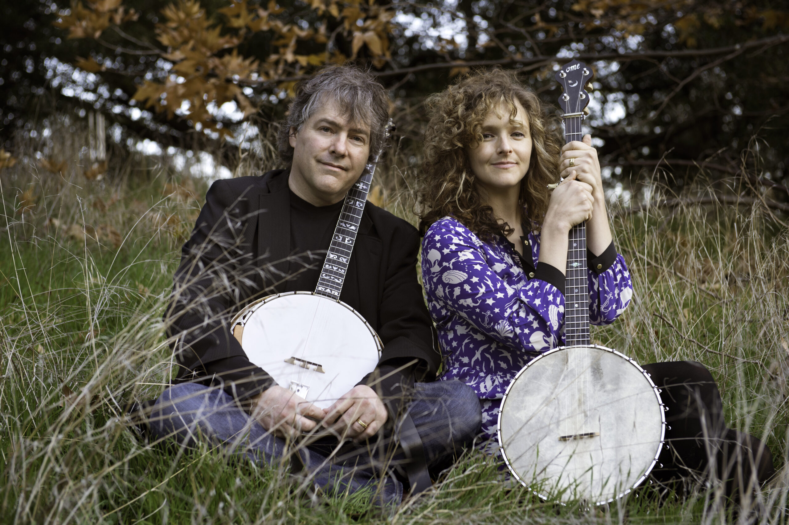 Abigail Washburn and Bela Fleck holding banjos while they sit together in a field.
