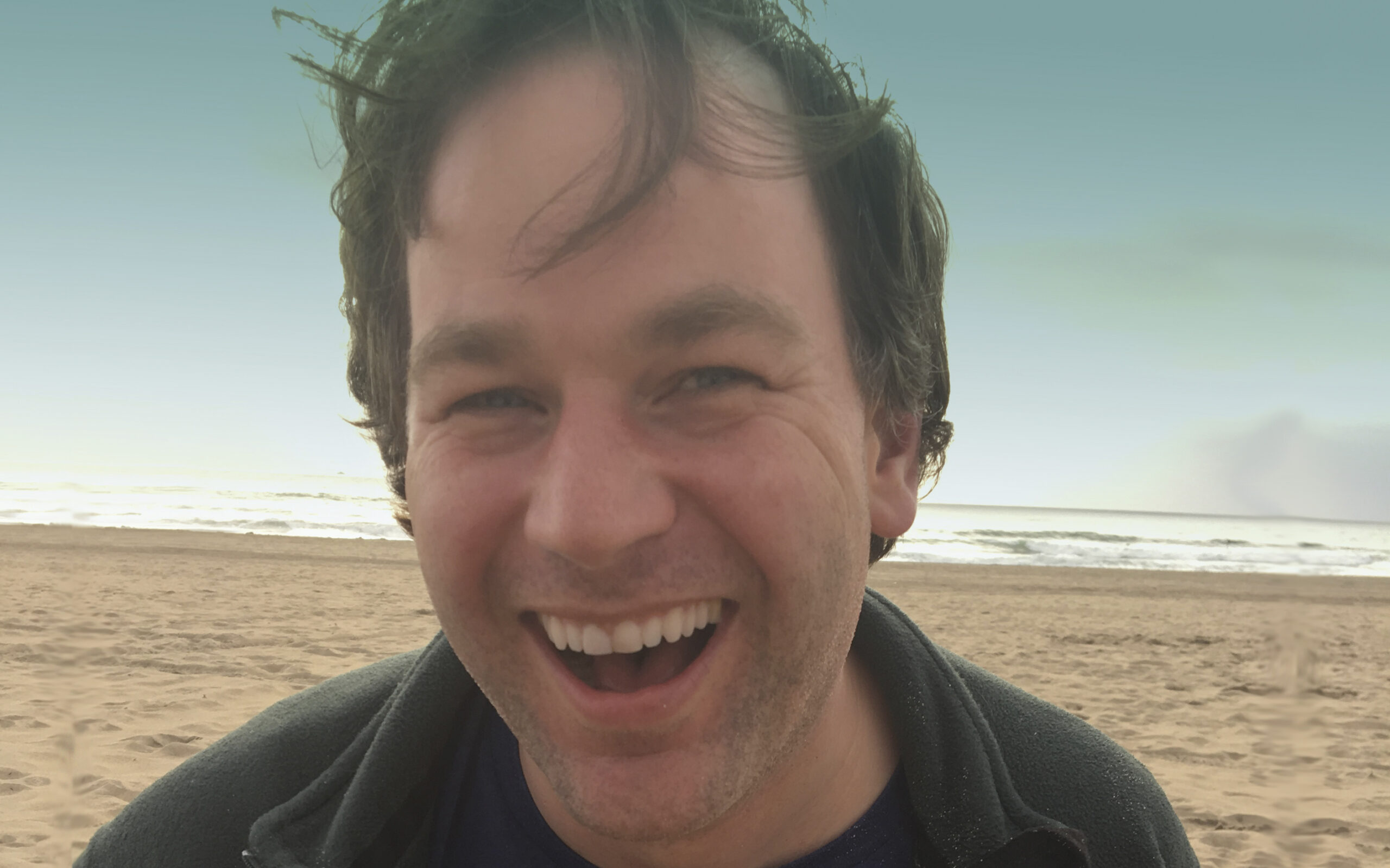 Mike Birbiglia at the beach laughing.