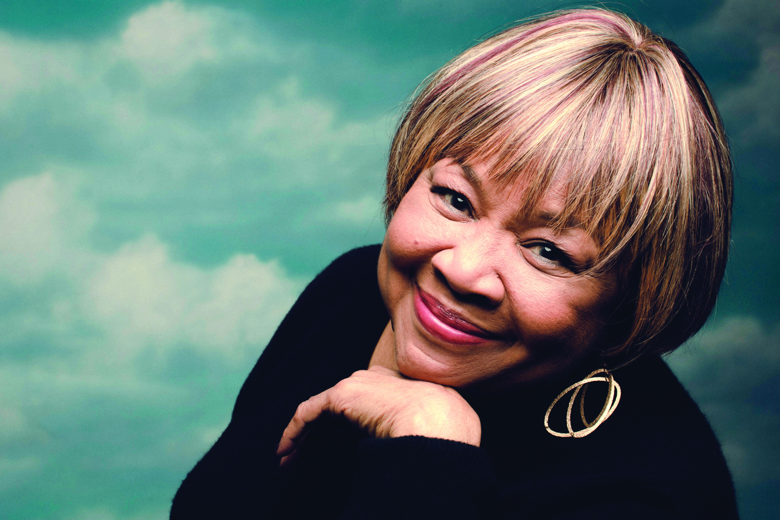 Mavis Staples smiling in front a cloudy sky.