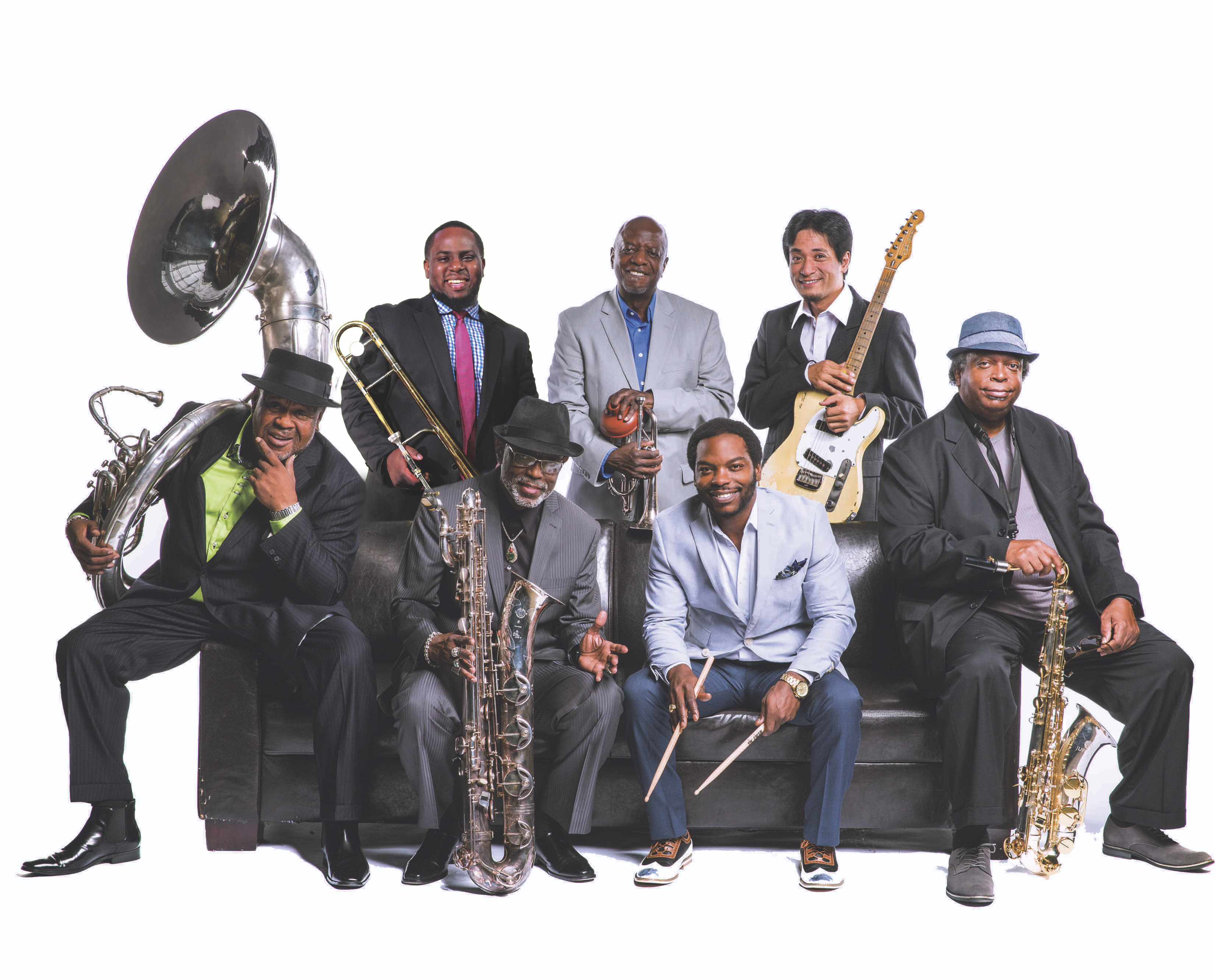 Members of the Dirty Dozen Brass band holding their instruments and smiling while sitting on a black leather couch.