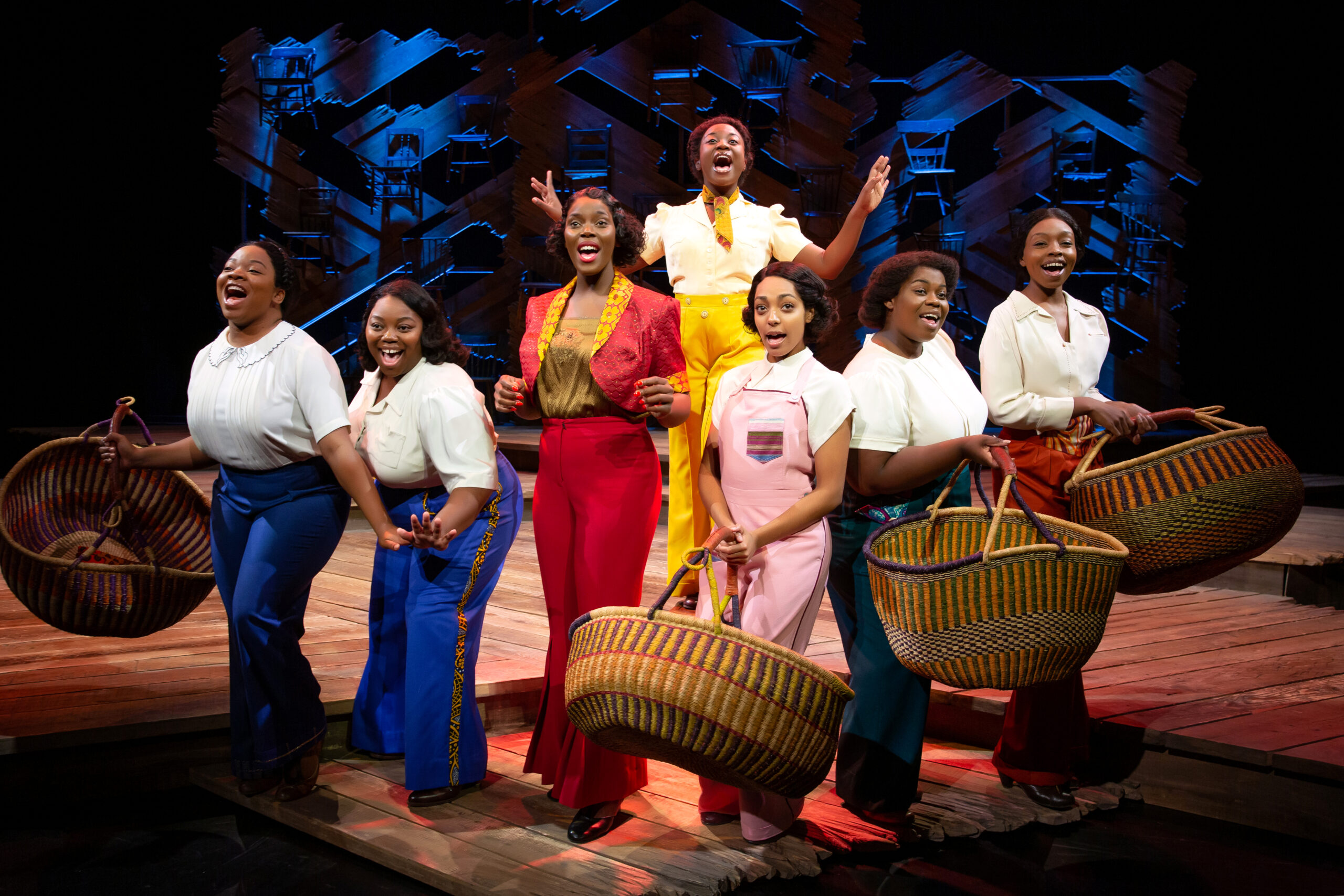 A cast photo of the women of The Color Purple singing happily.