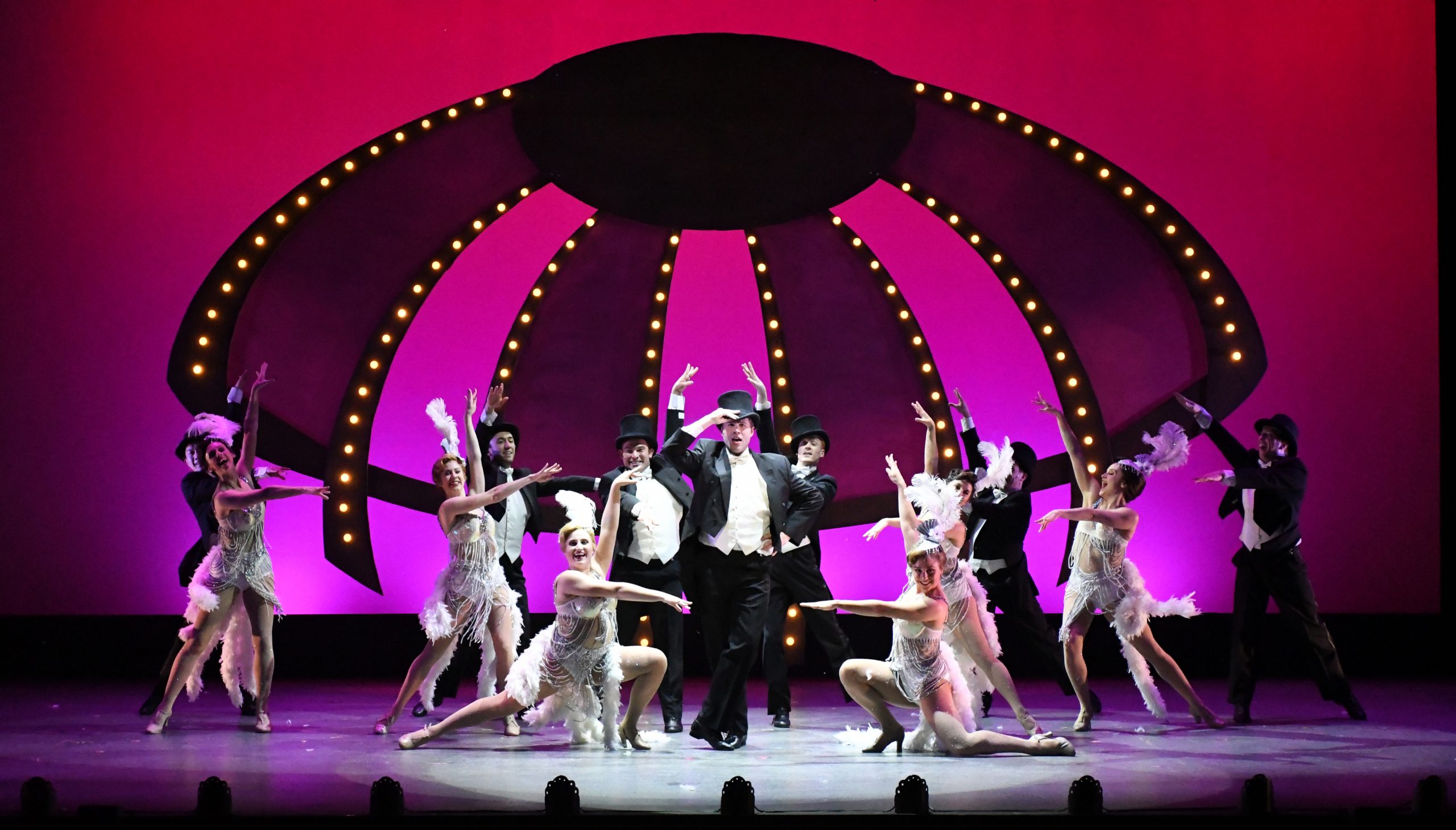 Jerry wearing a top hat and tuxedo in front of a Las Vegas style showgirl backdrop.