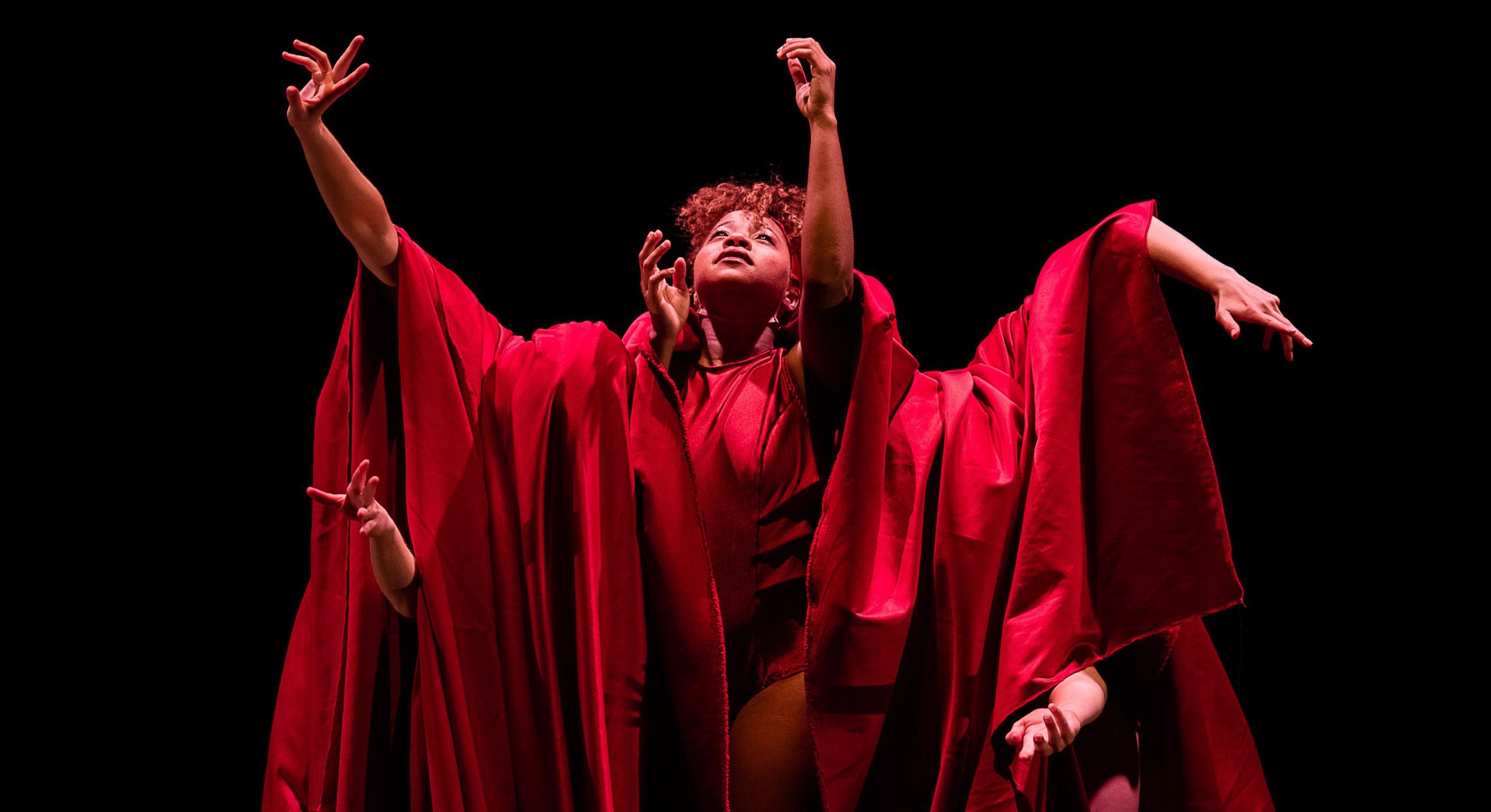Various dancers posed to look like a multi-armed red sculpture.
