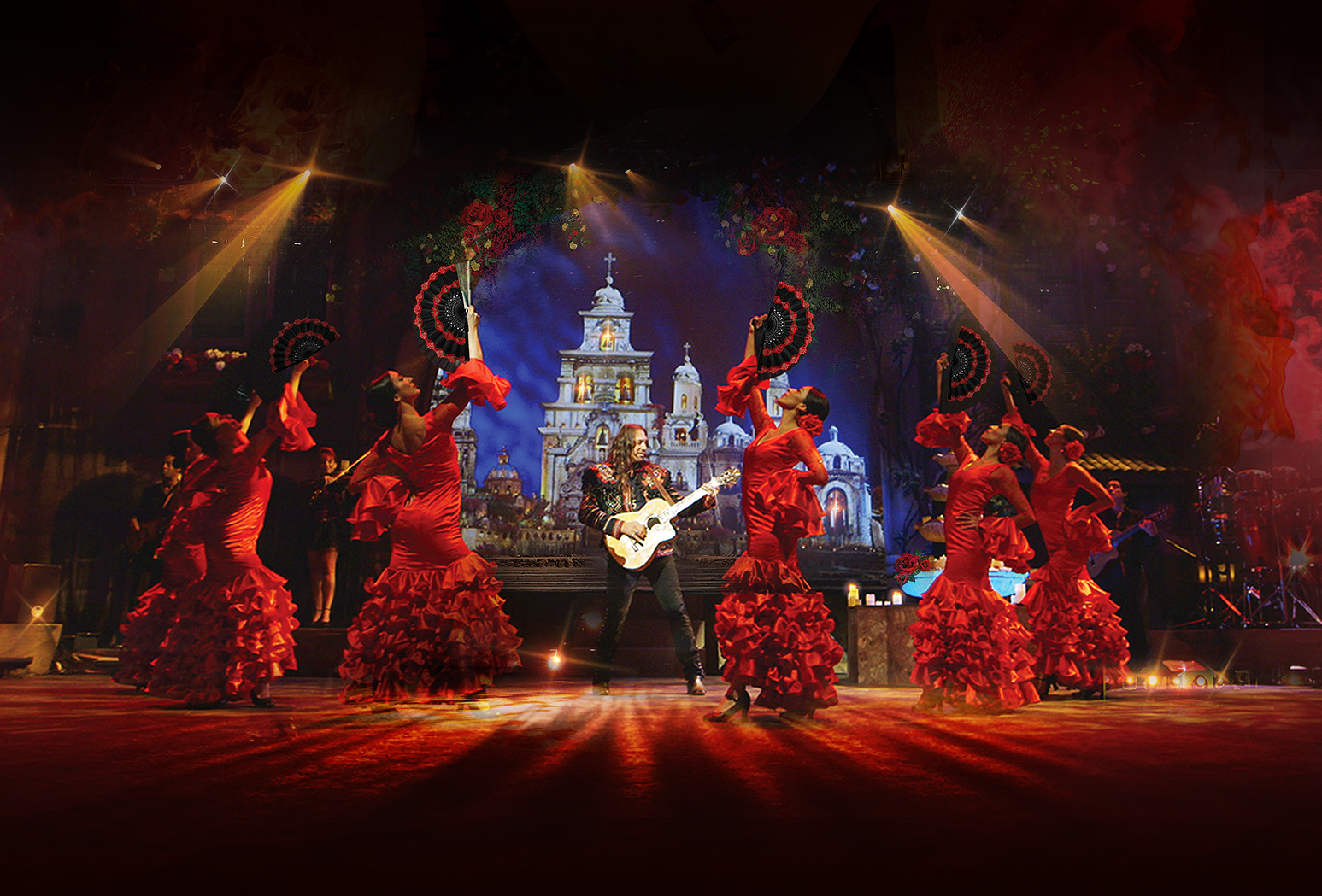 Six flamenco dancers in red holding fans surround Benise, who is playing an acoustic guitar.