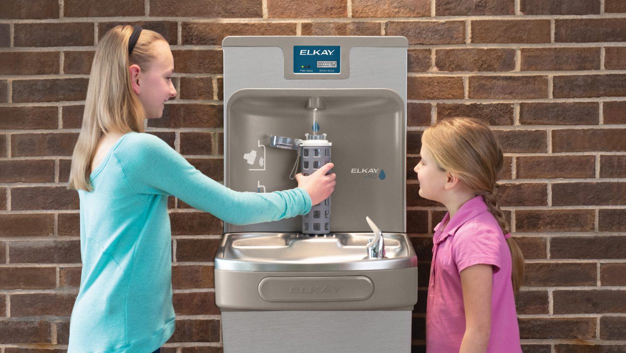 Two little girls filling a water bottle at the drinking fountain.
