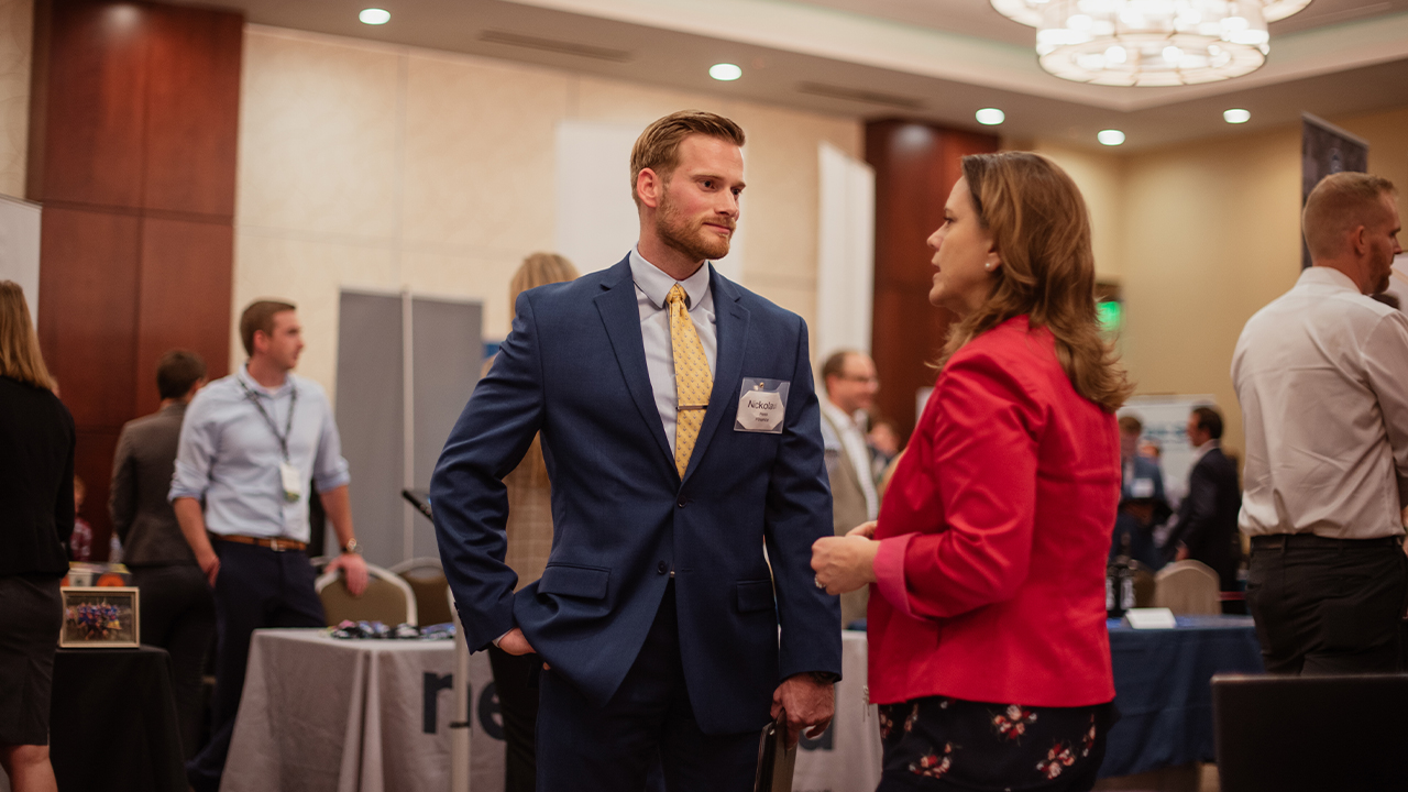 Man in a suit talking with a woman in red jacket at an job fair.