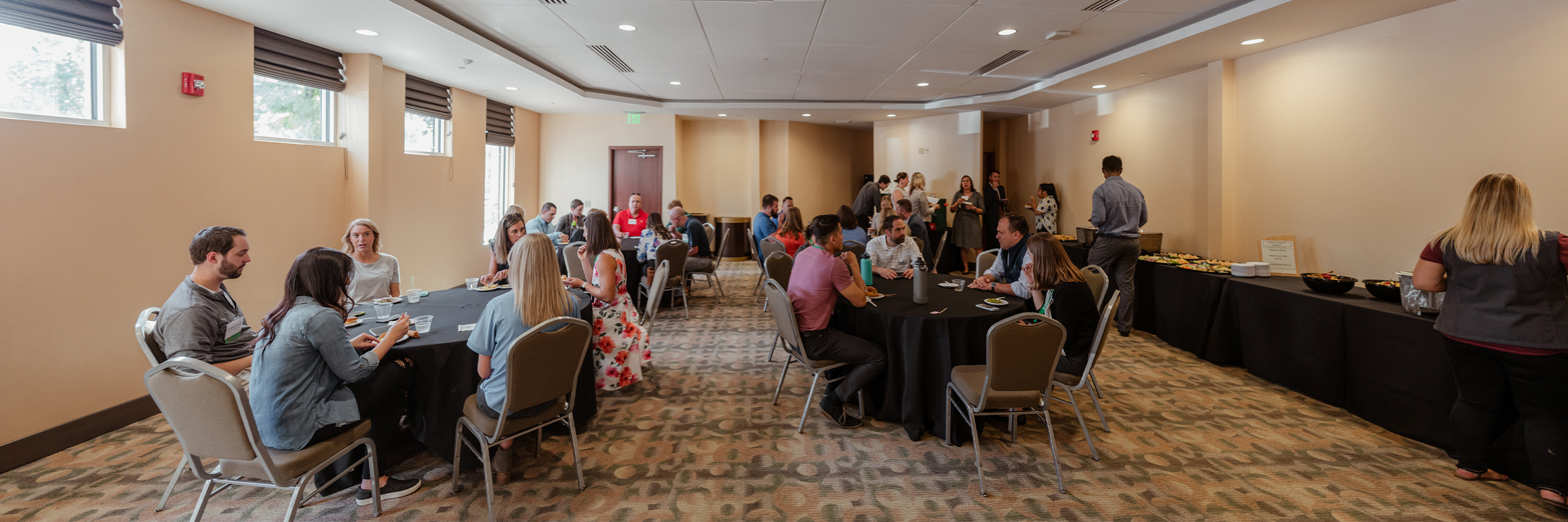 People get food from a buffet and enjoy lunch around round tables in the Founders Room.