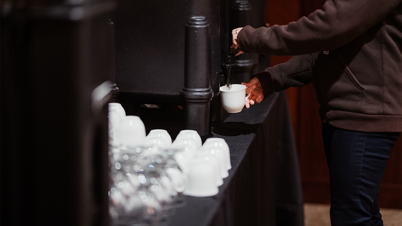 An attendee gets coffee from a table setup with cups and drink dispensers.