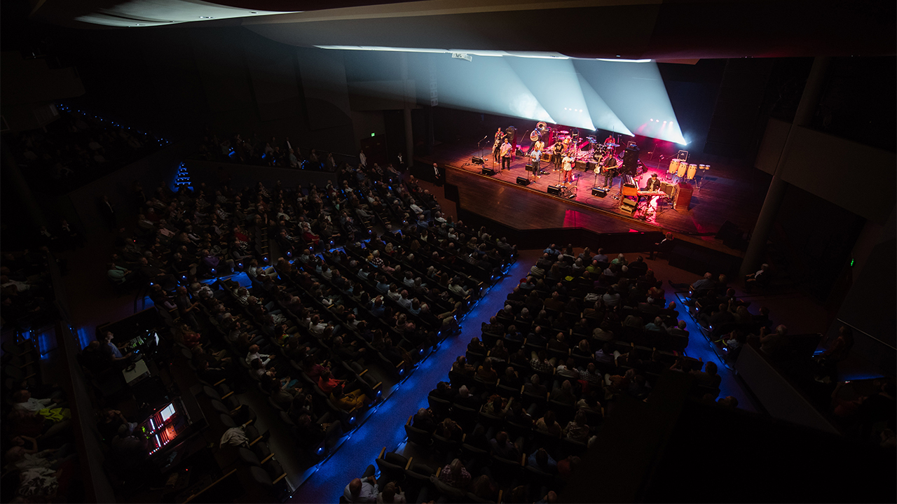 A band performs on stage to a full crowd in the Performance Hall.