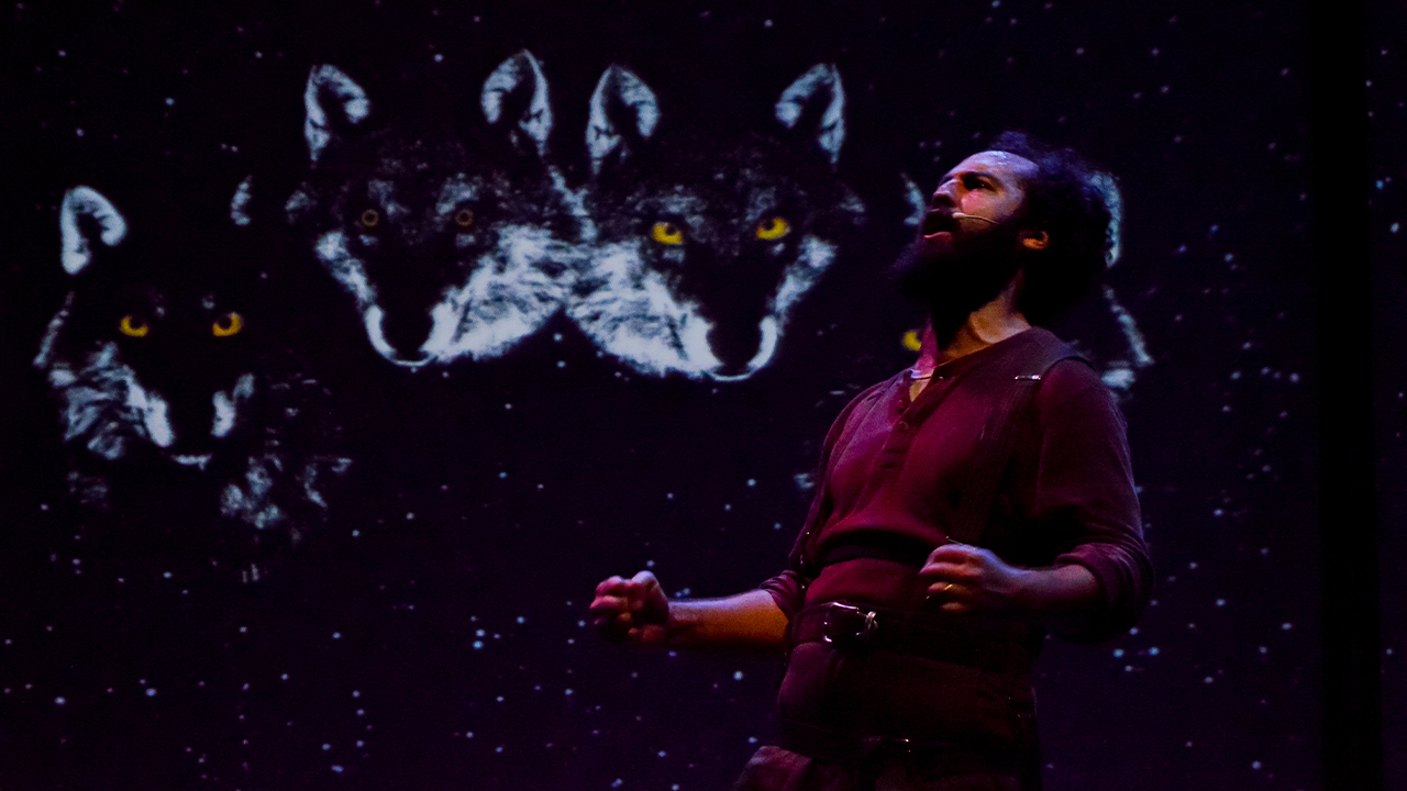 Man howling in front of a screen with three wolf heads.