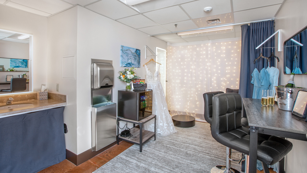 Dresses for a wedding hang in a spacious dressing room.