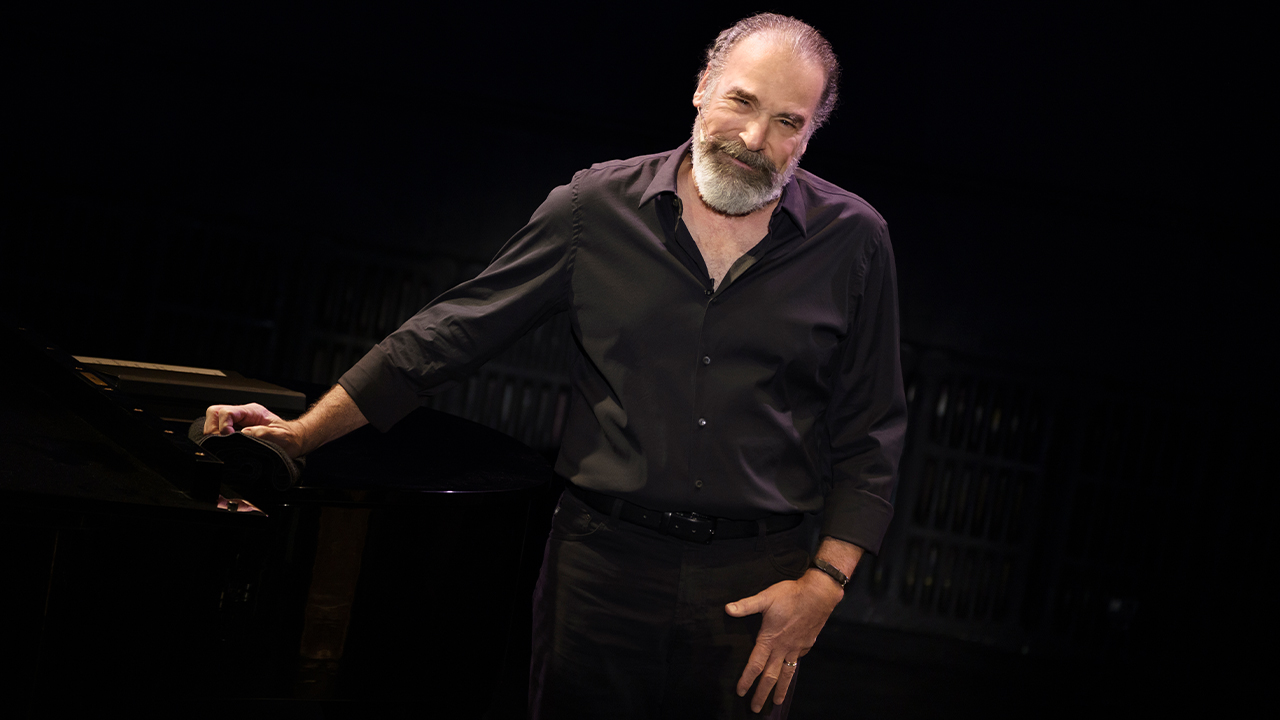 Mandy Patinkin standing next to a piano.
