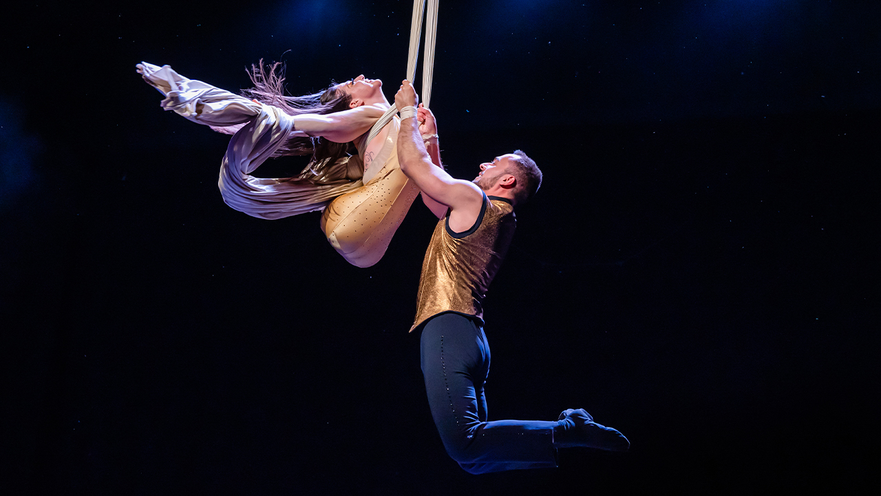 Omnium Circus performers in midair on a trapeze.