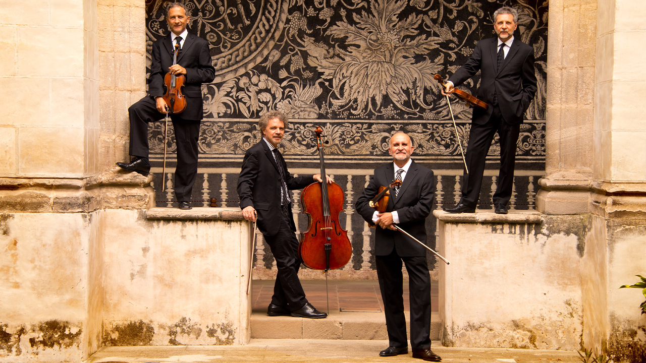 The members of Cuarteto Latinoamericano standing with their instruments in an archway.
