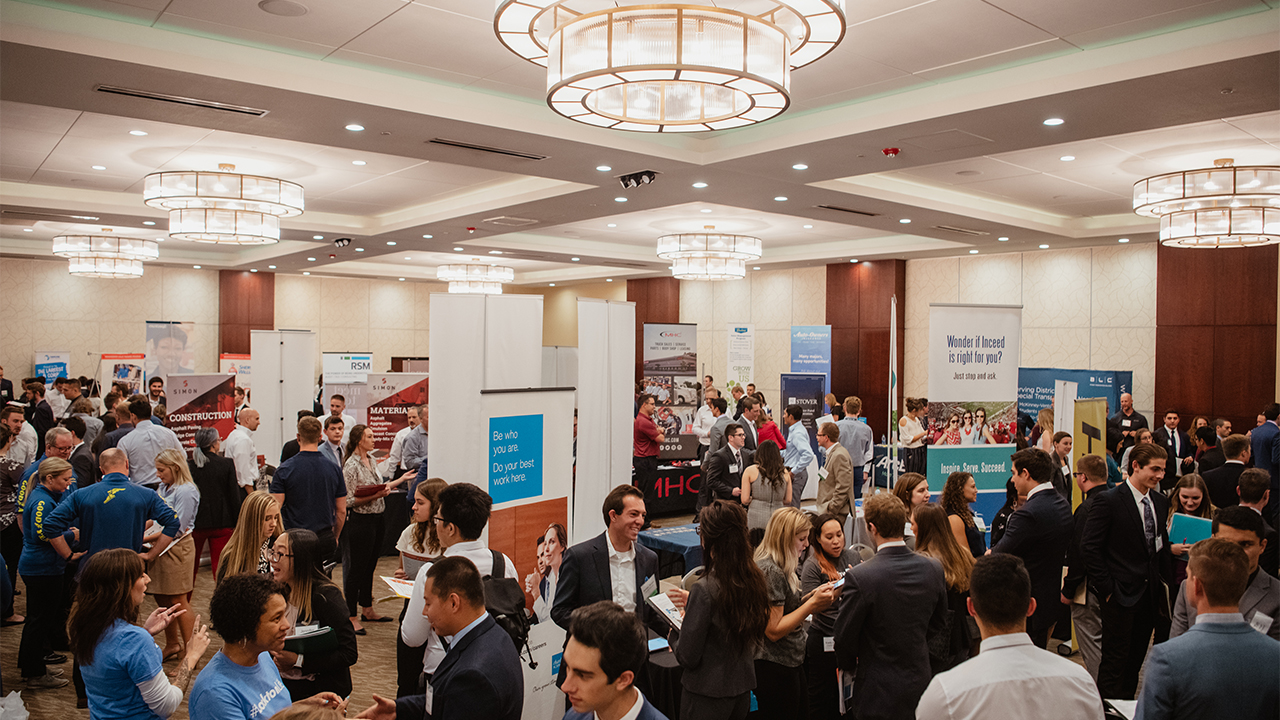 An expo takes place in Canyon West Ballroom with many vendors at tables speaking to attendees.