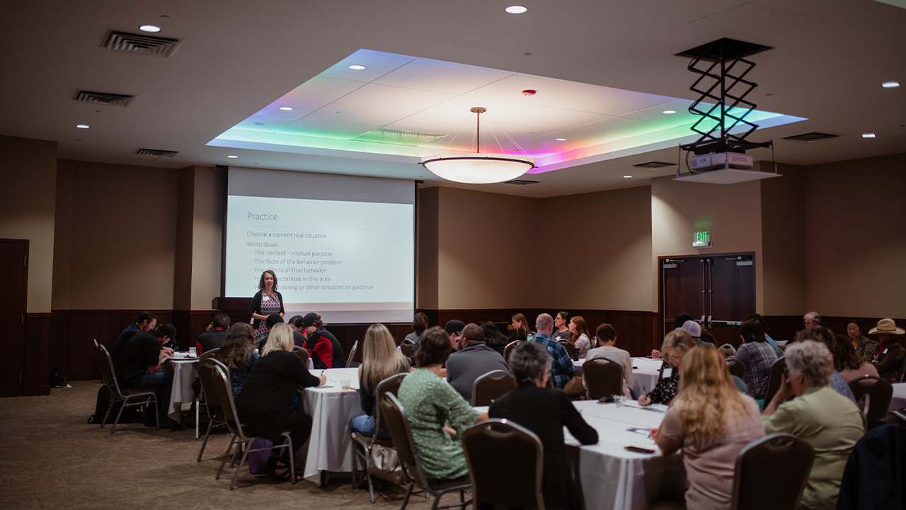 A women presents in front of a projection screen to conference attendees in the Columbine Room.