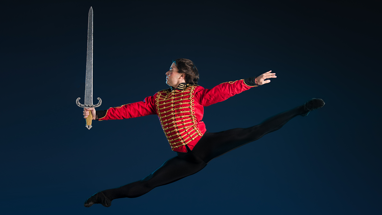 Dancer dressed as the Nutcracker mid-leap, holding a sword.