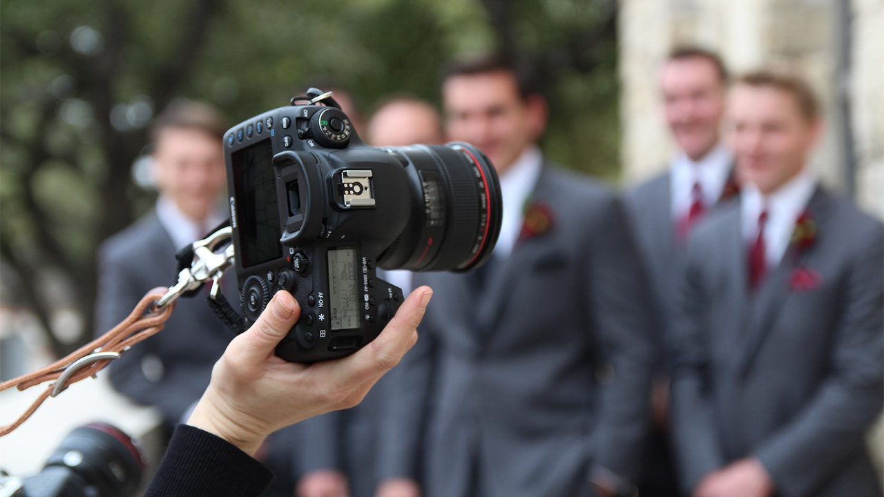 Person holding professional camera in front of wedding party. 