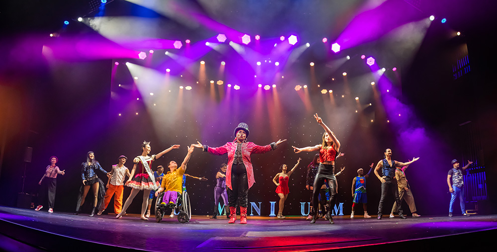 The full cast of Omnium Circus on stage, the ringmaster in the center with outspread arms.