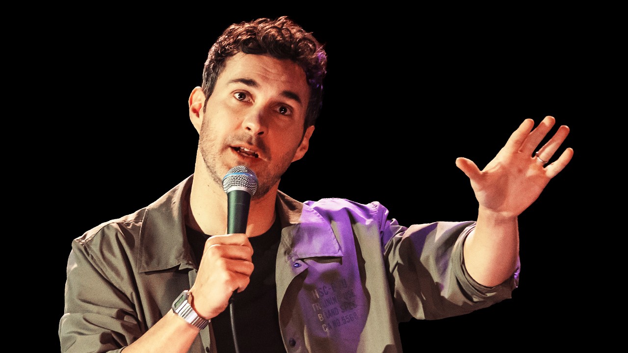 Mark Normand holding a microphone with his hand out.