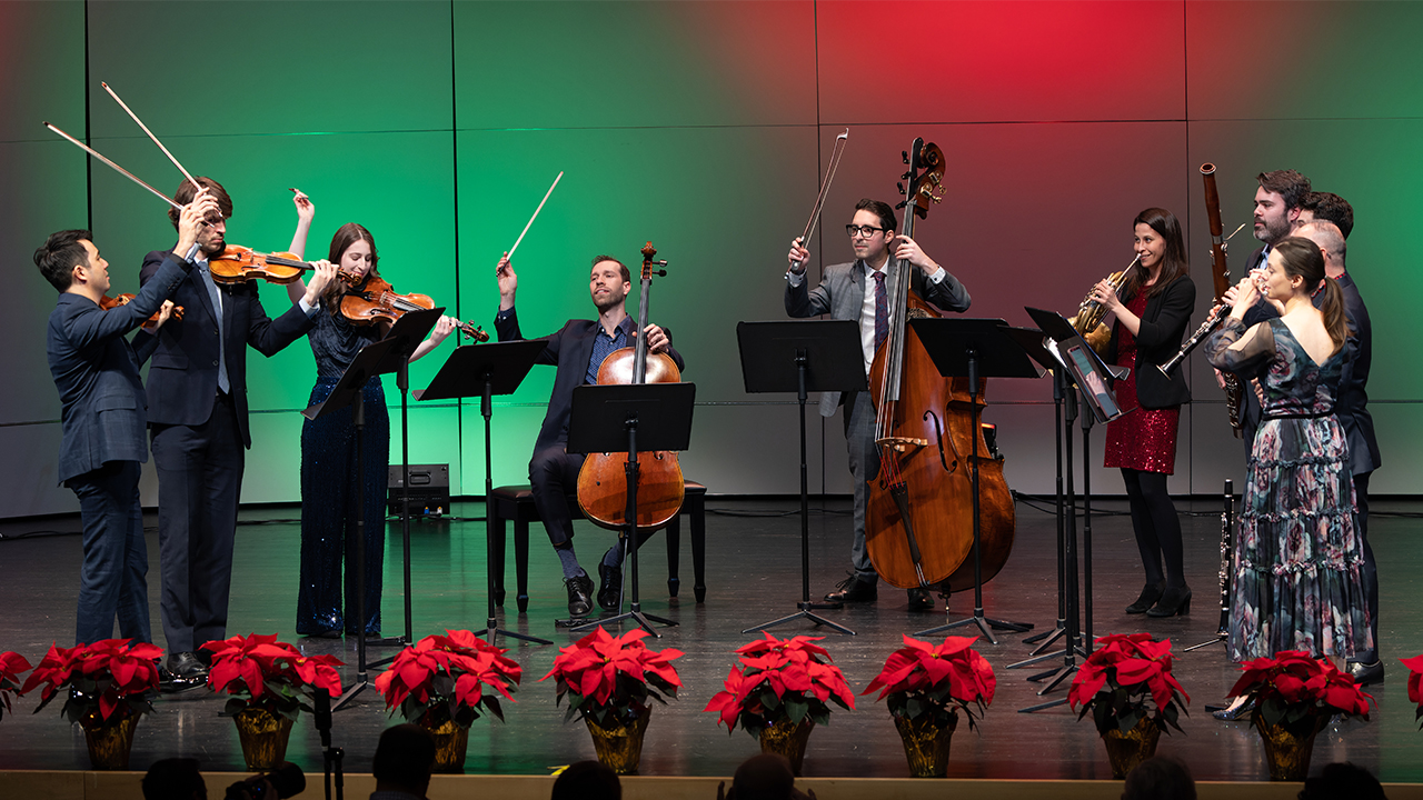 Frisson members playing on stage with green and red lighting and poinsettias