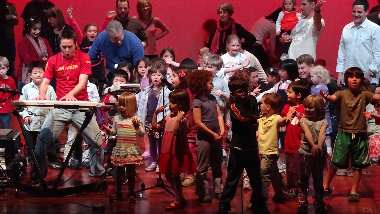 Dr. Noize singing with a group of kids on stage