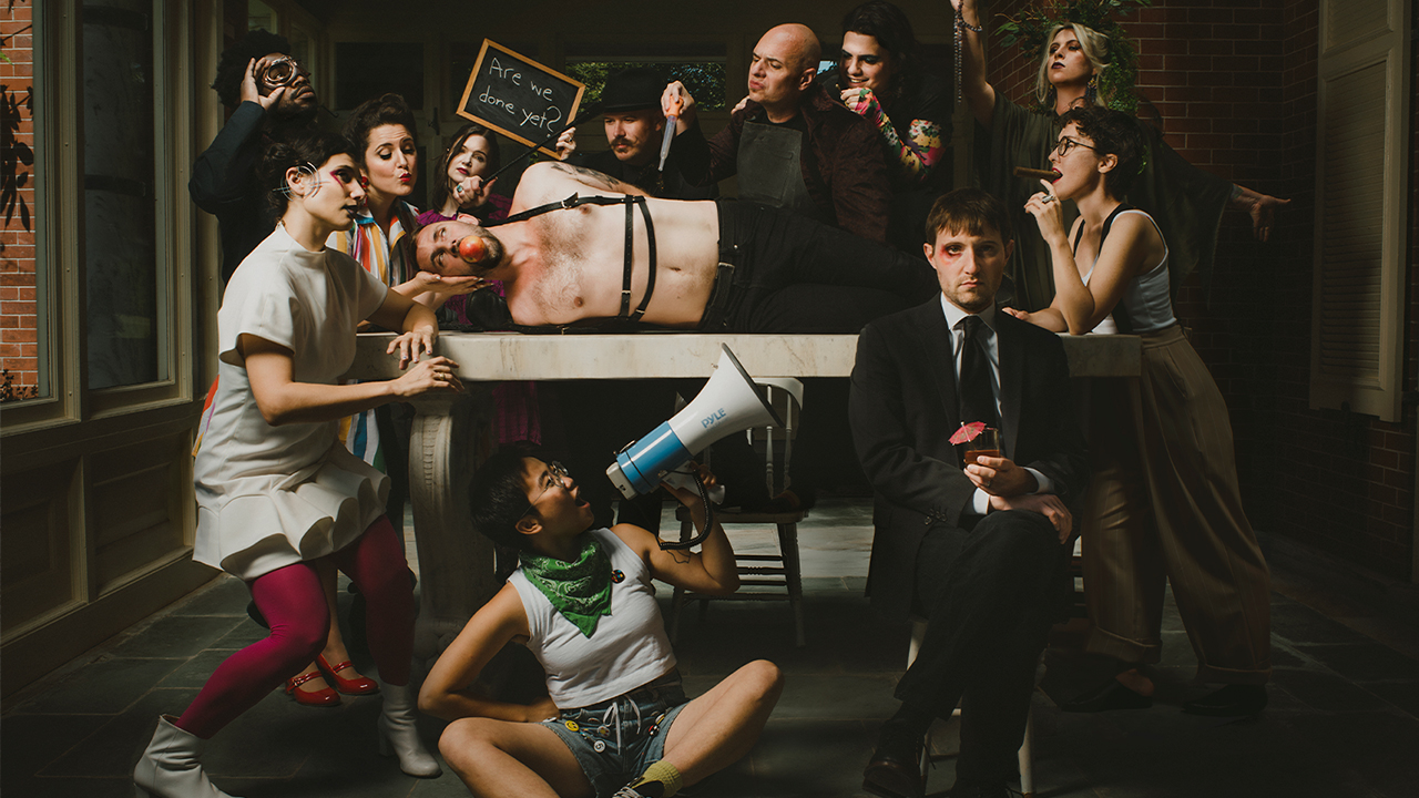 The vocal group surrounds one member on a table with an apple in his mouth