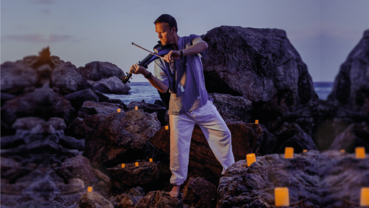 Man playing violin by candlelight on rocky beach