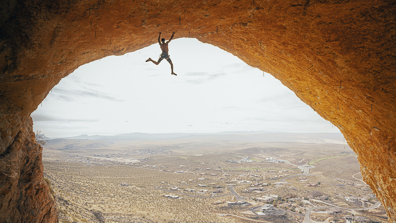 Photo of man climbing at the top of a large cavern overlooking a valley.
