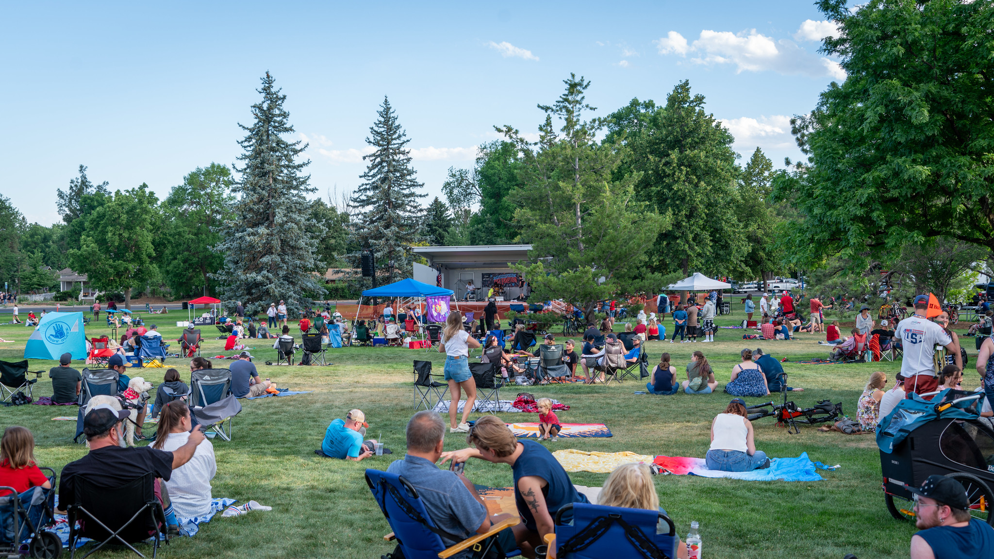 Groups of people sitting on picnic blankets facing an outdoor stage in City Park