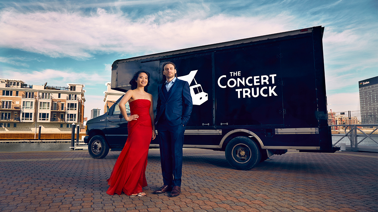 Nick Luby and Susan Zhang stand outside their converted 16-foot box truck in a formal dress and suit