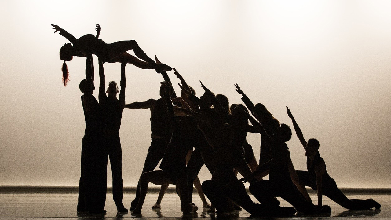 Dancers in silhouette lift another dancer into the air