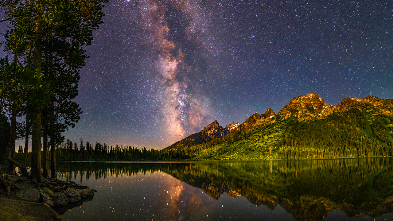 Image of the night sky reflected over a lake and mountains