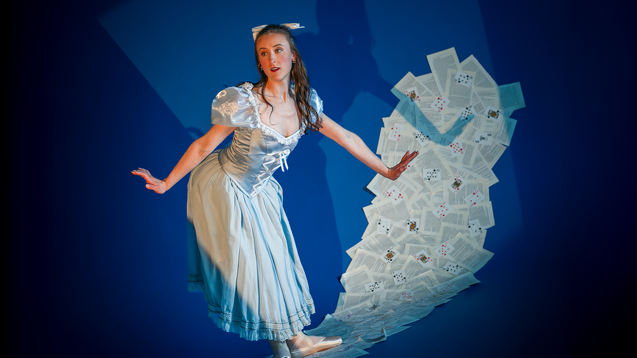 Ballet dancer Alice poses against a backdrop of playing cards and tossed papers