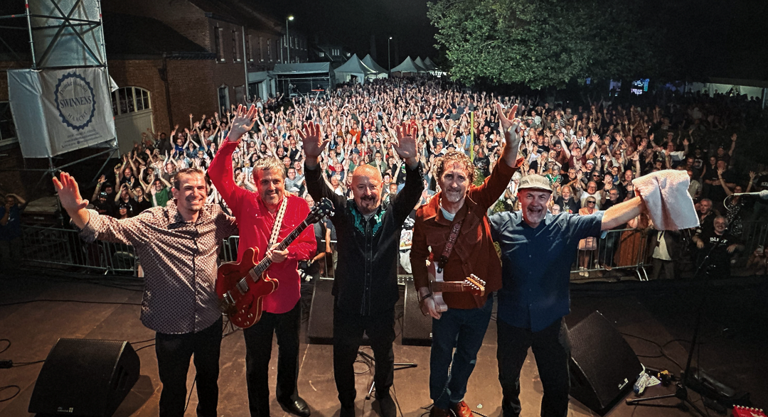 Members of The Fabulous Thunderbirds stand on stage a pose for a picture with their audience