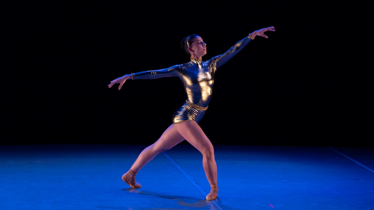 Ballerina dancing on a stage in a gold unitard and pointe shoes