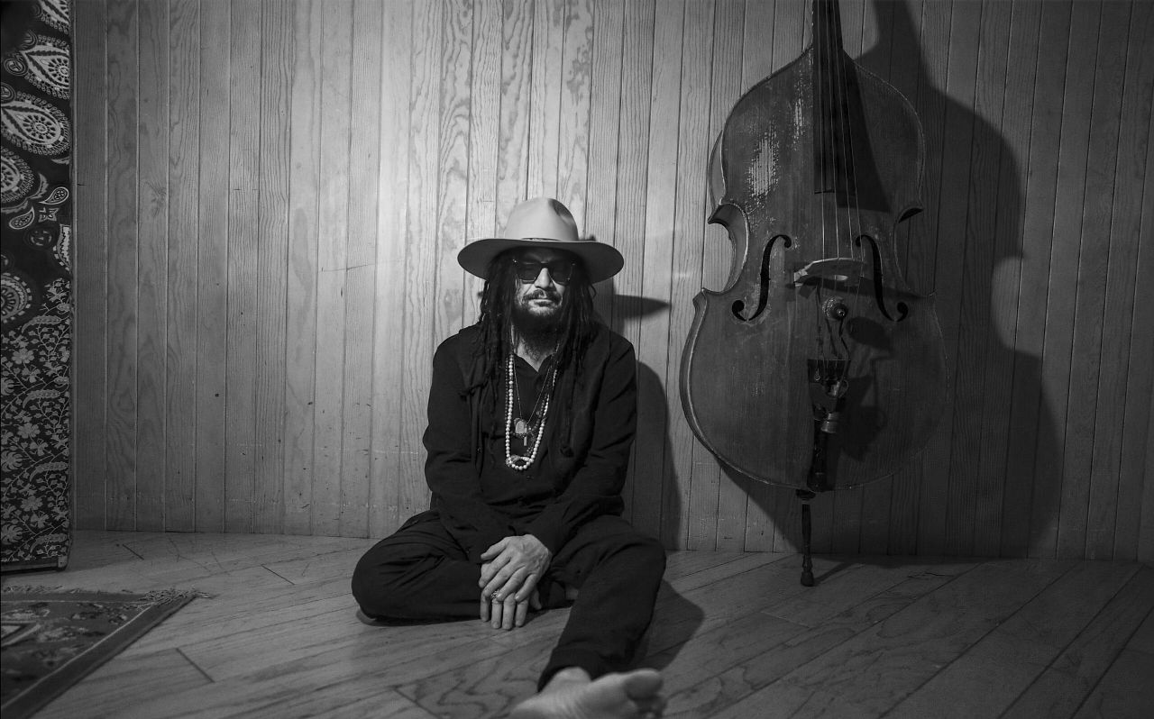 Don Was sits barefoot on the ground next to his stand-up bass