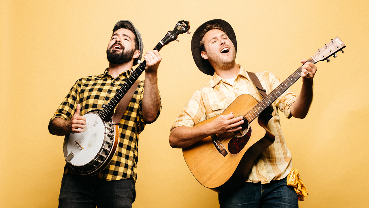 The Okee Dokee Brothers playing their guitar and banjo with a yellow background