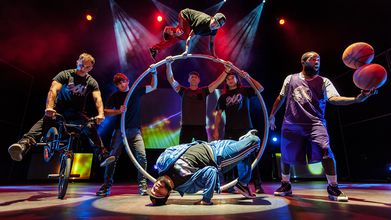 The performers on stage including a BMX rider, break dancer, basketball spinner, and aerial artist on a lyra hoop.