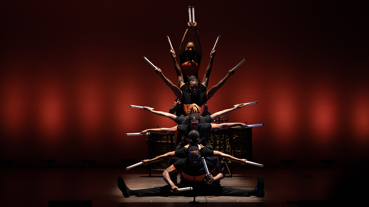 Members of Step Afrika creating a striking group pose with their arms held out holding batons