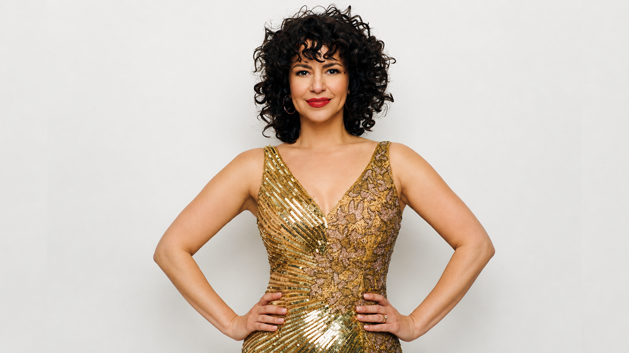 Image of Mandy Gonzalez in a gold dress with her hands on her hips